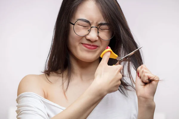 Verärgerte asiatische Mädchen haben Probleme mit langen Haaren, schneiden Spliss mit der Schere — Stockfoto