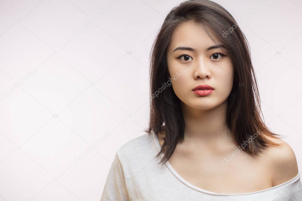 Calm beautiful Asian young woman with loose brown hair, isolated on white.