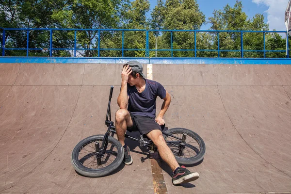 Rider sitting on BMX in skate park resting after riding — Stock Photo, Image