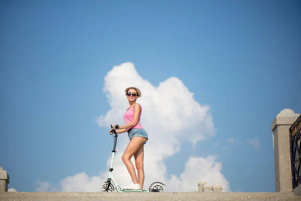 Mulher loira posando com azul chute scooter no fundo do céu — Fotografia de Stock