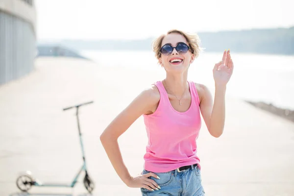 Chica impresionante en la calle de la ciudad en patinete scooter. Disfrutando de un día soleado. Usar gafas de sol, pantalones cortos — Foto de Stock