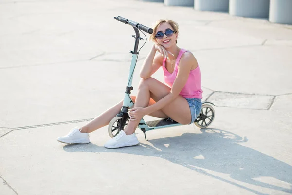 Femme blonde positive assise au scooter coup de pied bleu — Photo