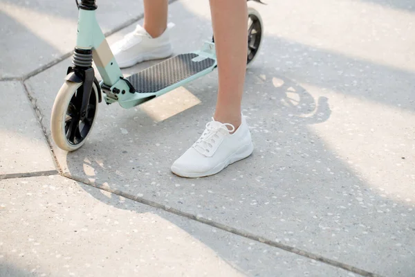 close up Woman legs on blue kick scooter on road at summer day