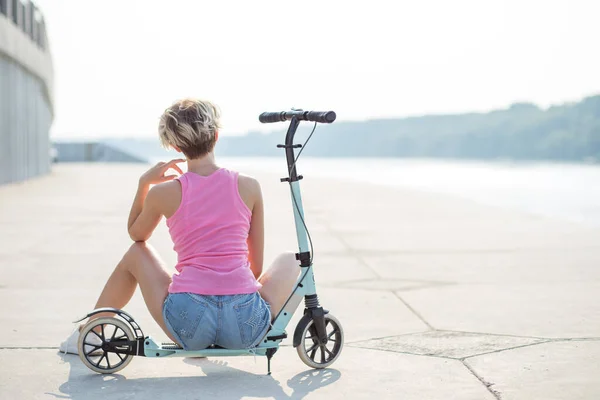 Positieve blonde vrouw zitten bij blauwe kick scooter — Stockfoto