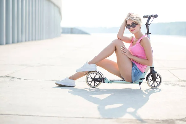 Mujer rubia positiva sentada en el patinete scooter azul —  Fotos de Stock