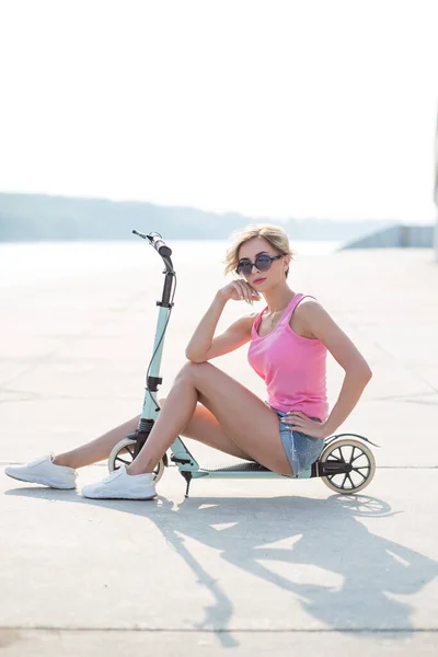 Mujer rubia positiva sentada en el patinete scooter azul —  Fotos de Stock