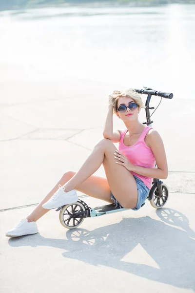 Mujer rubia positiva sentada en el patinete scooter azul — Foto de Stock