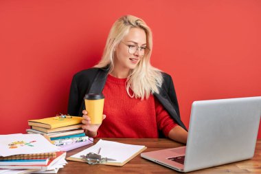 Genç bir kadın dizüstü bilgisayarla çalışırken kahve içer.