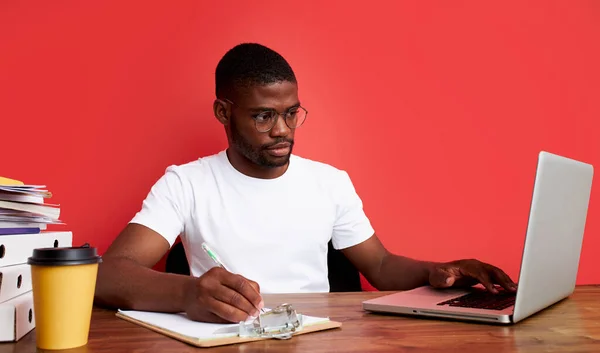 Ένας όμορφος Αφρο-Αμερικάνος σκέφτεται στη δουλειά, δουλεύει στο λάπτοπ. — Φωτογραφία Αρχείου