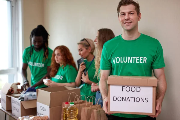 portrait of affable volunteer man in green t-shirt holding donation box in hands