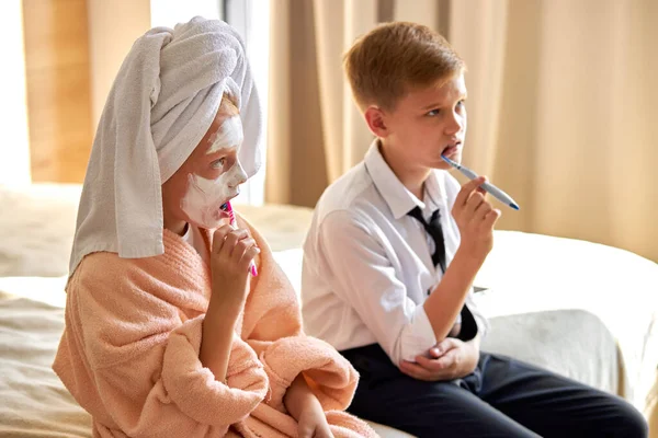 Niños somnolientos cepillándose los dientes por la mañana en la cama — Foto de Stock