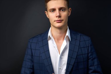 Siyah arka planda kameraya poz veren resmi takım elbiseli çekici bir adam.