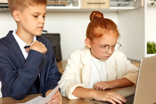 Кавказские дети вошли в роль взрослых, работают на ноутбуке с документами — стоковое фото