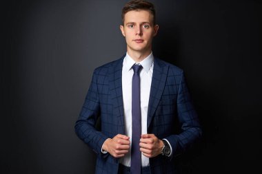 Siyah arka planda kameraya poz veren resmi takım elbiseli çekici bir adam.