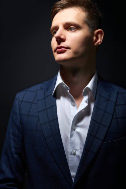 Siyah takım elbiseli düşünceli genç bir iş adamı siyah arka planda yalnız poz veriyor.