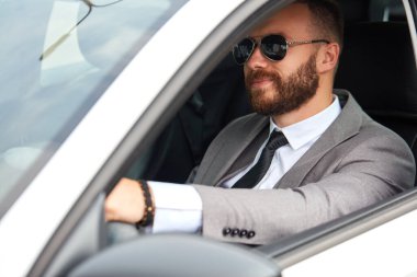 Resmi takım elbiseli başarılı bir beyaz adam araba kullanıyor.