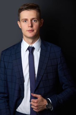 Siyah arka planda kameraya poz veren resmi takım elbiseli çekici bir adam.