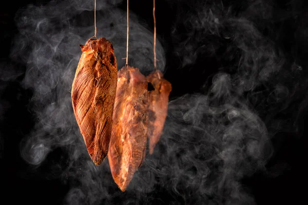 Carne branca de frango defumada no processo de fumar em um fundo preto Imagem De Stock