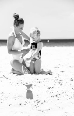 Aile eğlence beyaz kum üzerinde. Closeup spf şişesini sahil ve anne ve kızı arka planda mayo