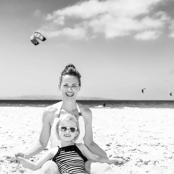 白い砂の上の家族の楽しみです 海辺に座ってビーチウェアは幸せなモダンな母と子 — ストック写真