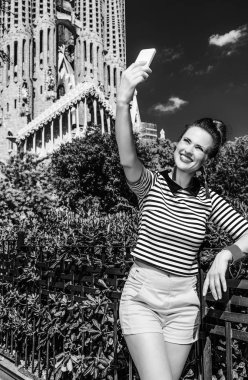 Barcelona - 10 Temmuz 2017: şık gezgin kadın şort ve selfie alarak smartphone ile karşı Sagrada Familia için Barselona, İspanya, çizgili gömlek