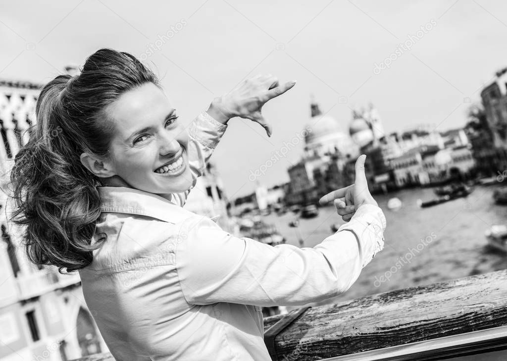 happy young woman framing with hands while standing on bridge with grand canal view in venice, italy