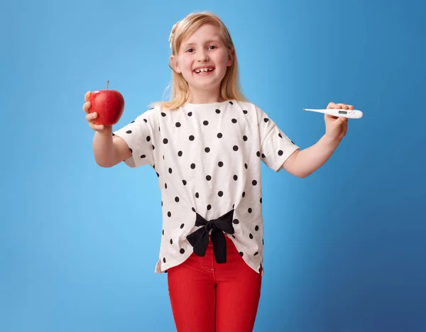 Úsměvem Moderní Dítě Červených Kalhotách Zobrazující Jablko Teploměr Modrém Pozadí — Stock fotografie