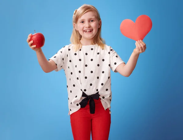 Úsměvem Moderní Dítě Červených Kalhotách Ukazující Papírové Srdce Apple Modrém — Stock fotografie