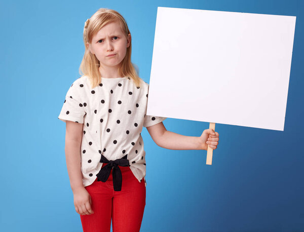 unhappy modern girl in red pants showing blank poster against blue background