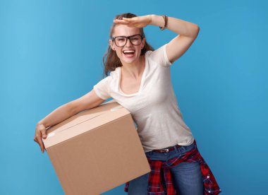 mavi arka plan karşı mesafe bakarak bir karton kutu ile beyaz gömlek gülümseyen etkin hipster