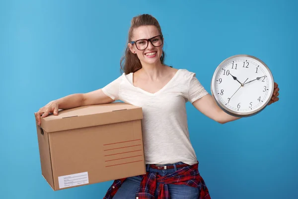 happy hipster in white shirt with a cardboard box showing clock against blue background