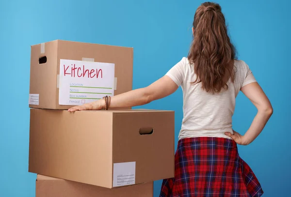 从后面看到的白色衬衫的现代妇女站在旁边的纸板盒蓝色背景 — 图库照片