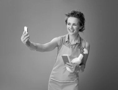 Mutfak sünger ile bir önlük ve deterjan selfie smartphone ile alarak bir şişe modern ev kadını gülümseyen