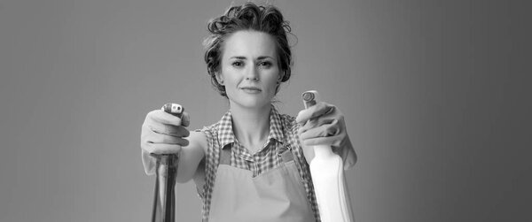 жизнерадостная молодая домохозяйка в резиновых перчатках с использованием бутылок моющих средств в качестве оружия
 