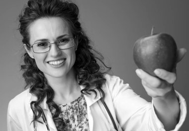 Çocuk doktoru bir elma veren beyaz tıbbi elbise içinde gülümseyen