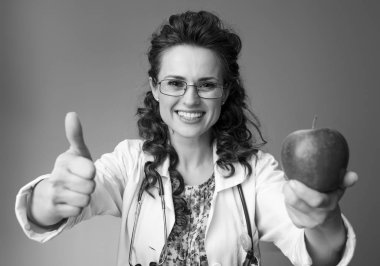 Çocuk doktoru Doktor bir elma veren ve arka plan üzerinde başparmak gösterilmesini beyaz tıbbi elbise içinde gülümseyen