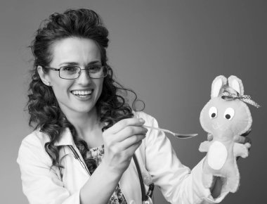 Çocuk doktoru Doktor üzerinde izole bir oyuncak bir kaşık çocuk süspansiyonun vererek beyaz tıbbi elbise içinde gülümseyen