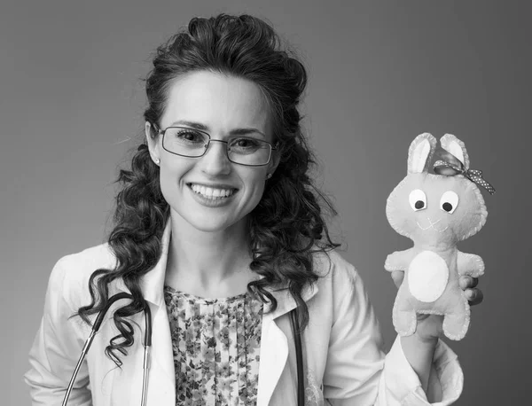 Çocuk doktoru Doktor oyuncak arka plan karşı gösterilen beyaz tıbbi elbise içinde gülümseyen