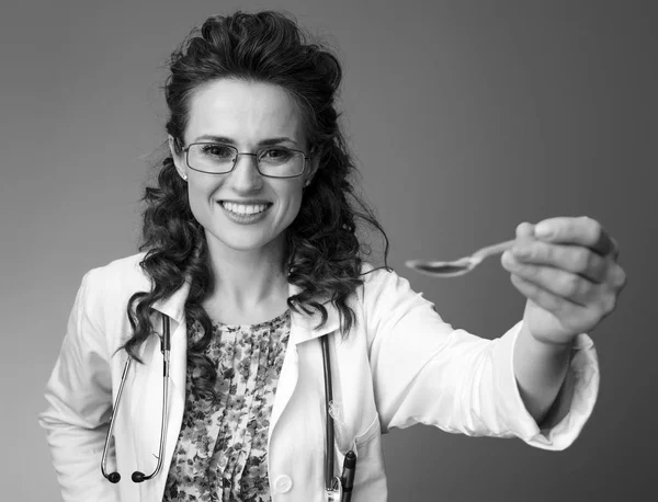 gülümseyen paediatrist kadın çocuk süspansiyon arka plan karşı bir kaşık veren beyaz tıbbi elbise içinde