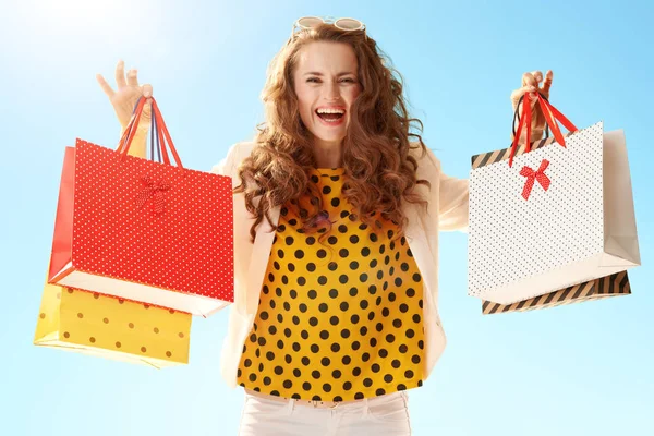 Lycklig Trendiga Kvinna Ljus Jacka Visar Shoppingkassar Mot Blå Himmel — Stockfoto