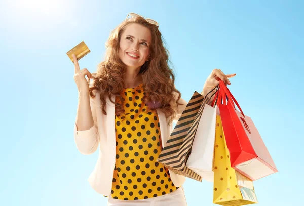 沉思时尚的女人穿着轻便夹克 购物袋和信用卡对蓝天 — 图库照片