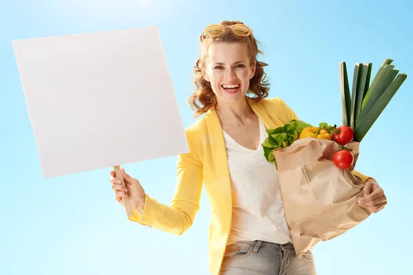 Glückliche Moderne Frau Gelber Jacke Mit Papiertüte Mit Lebensmitteln Zeigt — Stockfoto