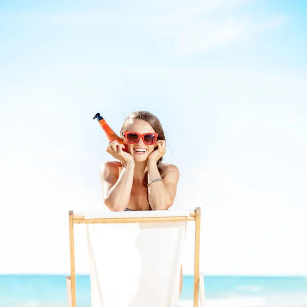 Spf を押しながらビーチの椅子に座っての海岸で水着で笑顔の若い女性 — ストック写真