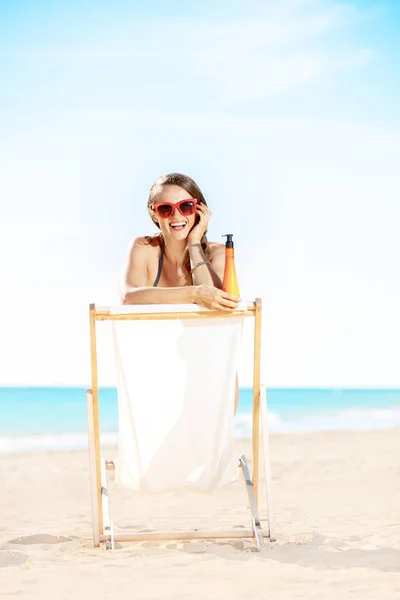 ビーチチェアに座っている日焼け止めローション海岸の水着で幸せな現代の女性 — ストック写真