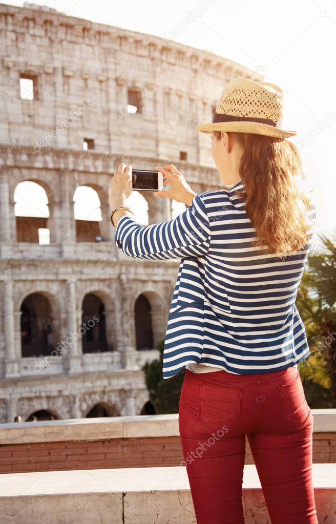 Seen from behind young tourist woman in a striped jacket in Rome, Italy taking photo with smartphone
