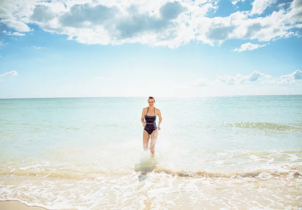 海が不足している海岸のビーチウェアの笑顔の現代の女性の完全な長さの肖像画 — ストック写真