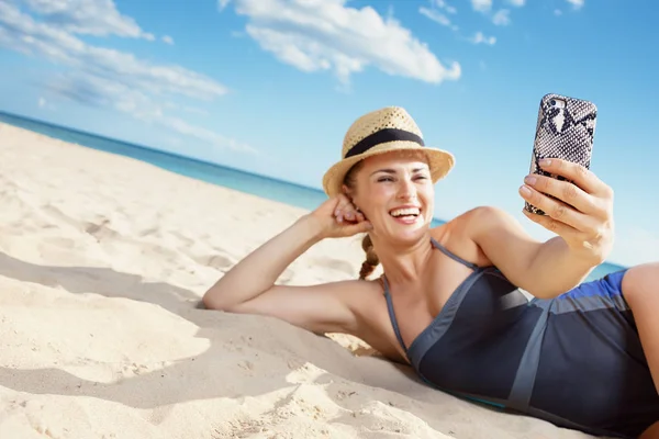 水着で海岸でスマート フォンで Selfie を取って幸せな若い女にクローズ アップ — ストック写真
