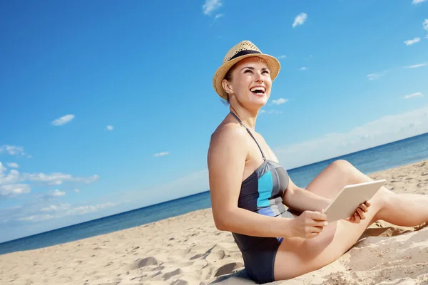 happy modern woman in swimwear with tablet PC looking into the distance on the seacoast