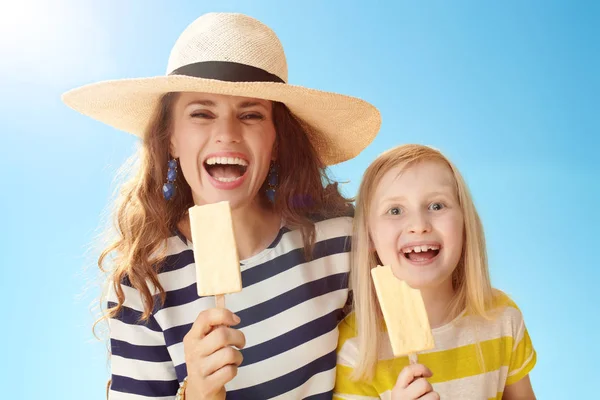 微笑的年轻母亲和女儿用冰淇淋对蓝天的棍子 — 图库照片