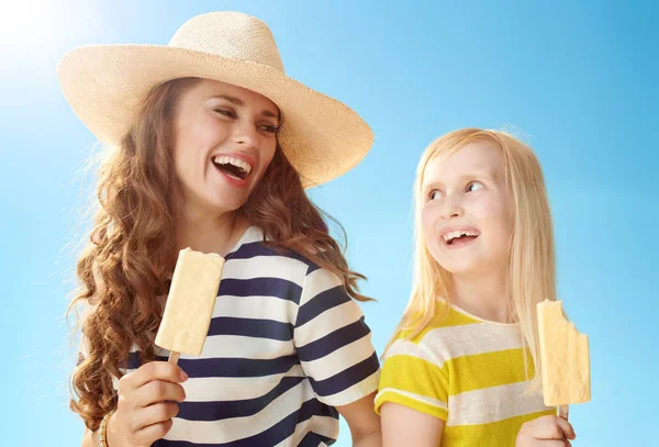 幸せな若い母と娘は青い空を背景にお互いを見て棒のアイスクリーム — ストック写真